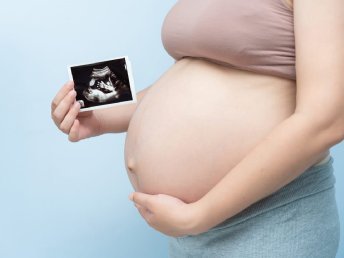 Pregnant woman in the third trimester holding an ultrasound image from a growth scan.