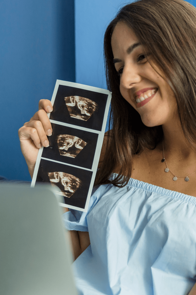 Smiling lady joyfully displaying her ultrasound (USG) image.
